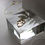 Thumbnail: Gold necklace on a clear, resin square prop with muted light.
