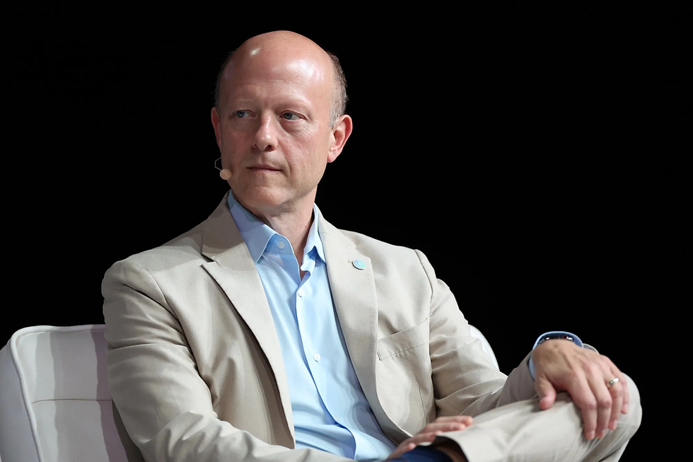 Circle co-founder and CEO Jeremy Allaire in a beige suit with a blue shirt, wearing a lapel pin, sits on stage with a microphone earpiece. Dark background, focused expression.
