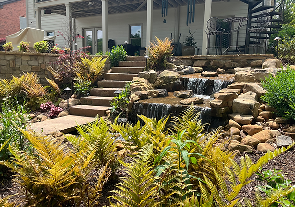 a stone staircase leading to a stone walkway towards the lake with a boulder waterfall feature and lush planting surrounding in Alpharetta, GA