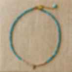 Minimalist kyanite gemstone necklace with pink pearls and gold sun pendant on artisan burlap.