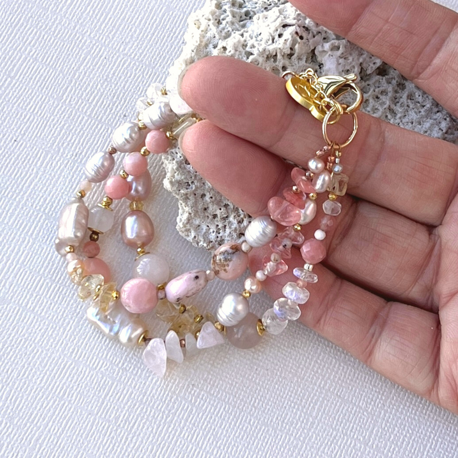 Pink Peruvian Opal and Pearl Gemstone Bracelet featuring three strands of pink gemstones and pink pearls held in a hand.