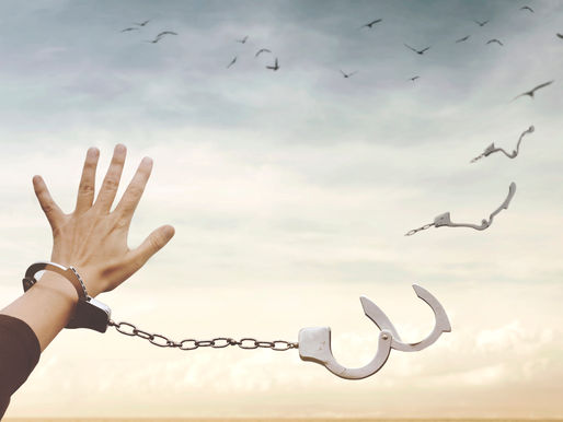 Hand breaking open a handcuff chain against a bright sky with birds flying, symbolizing freedom.
