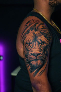 Realistyczny tatuaż głowy lwa w czarno-szarej stylistyce na ciemnej skórze