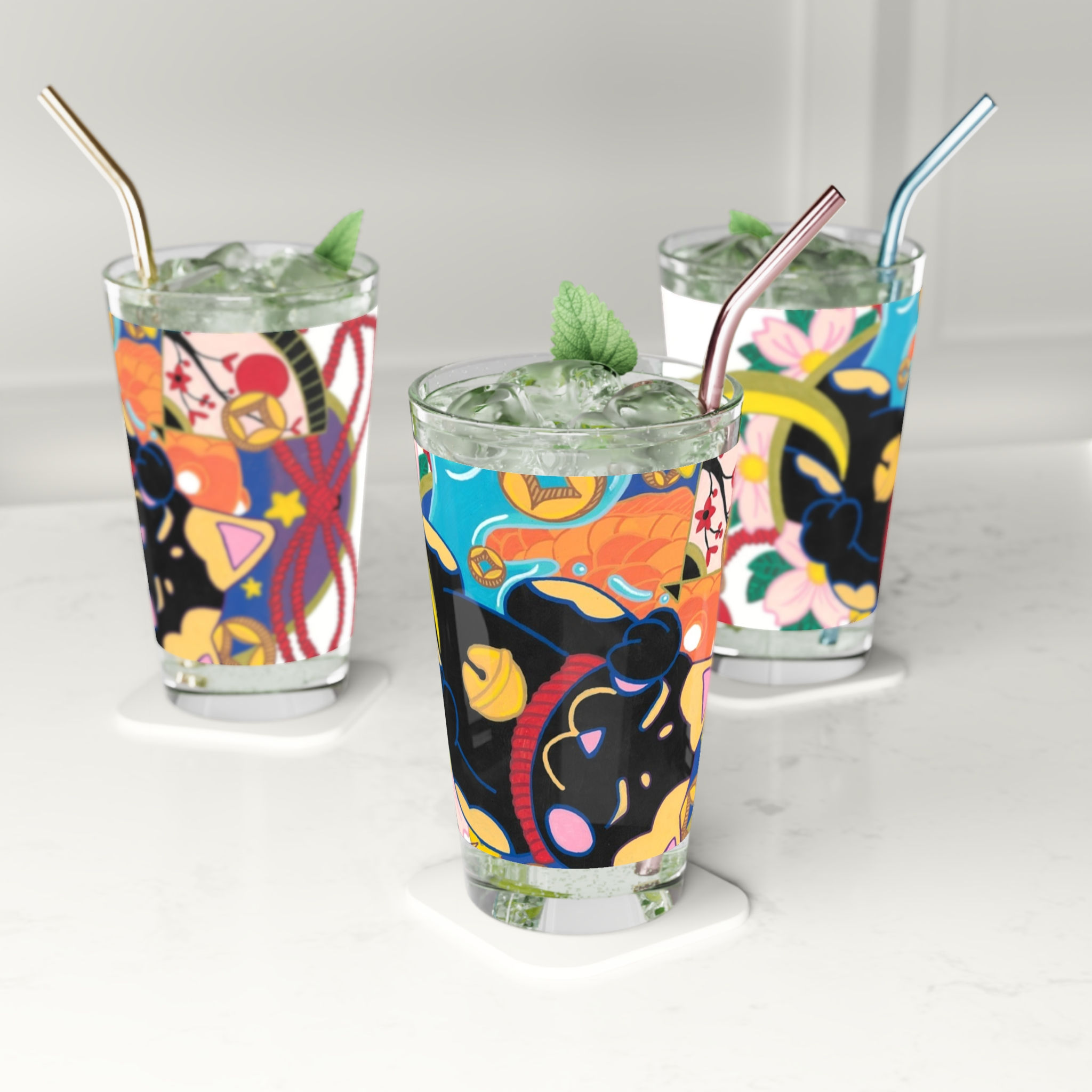 Three glasses with vibrant graphic designs, green drinks, mint, and metal straws
