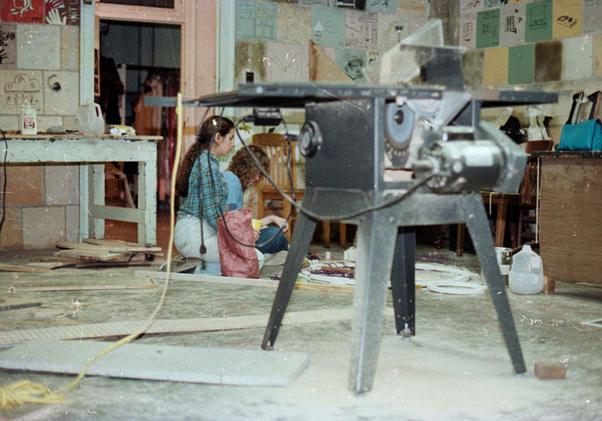 Caucasian woman and man sitting on the ground in wood shop classroom.