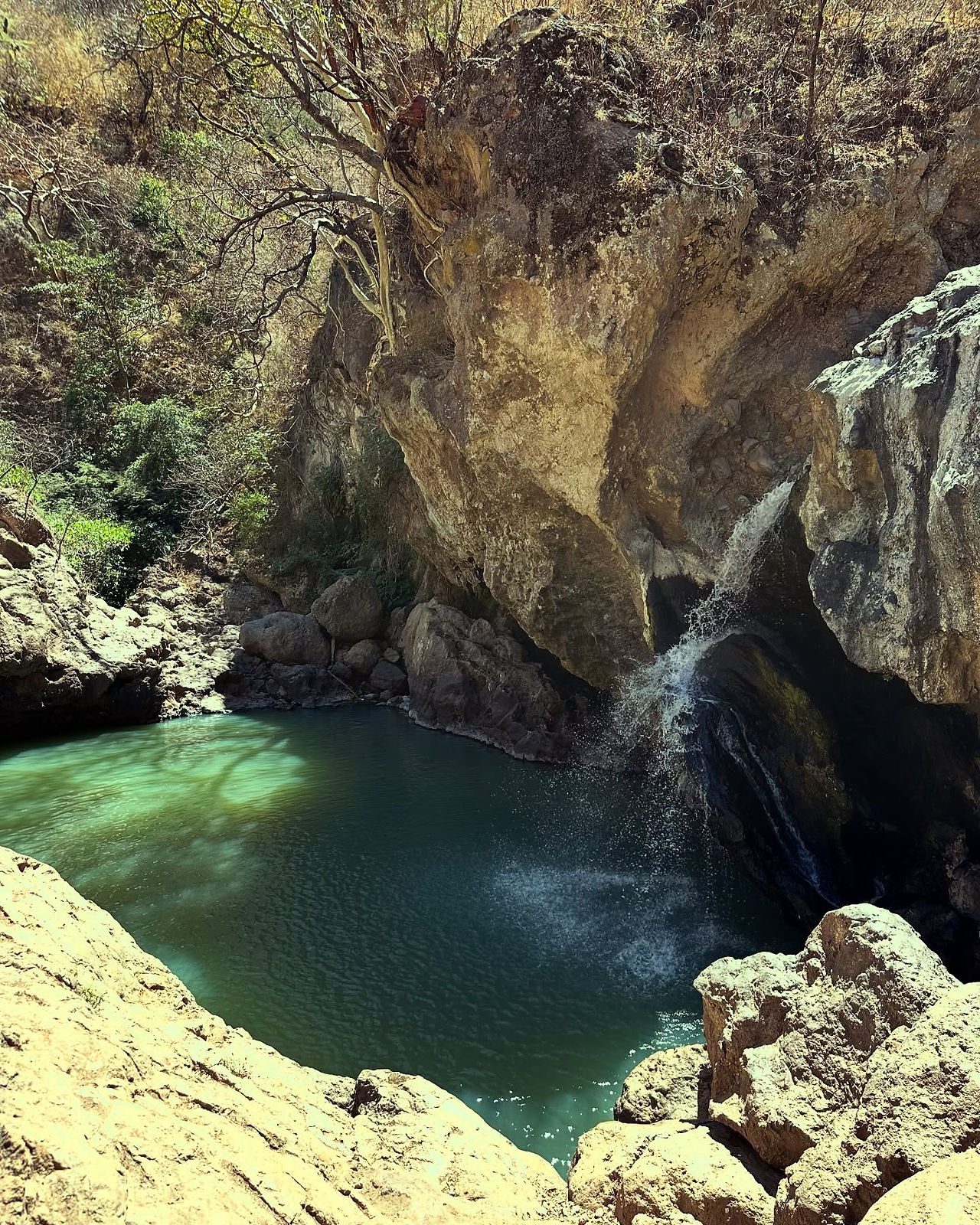 Cascada de Huaxla formando una charca de agua verde rodeada de piedras y vegetación.