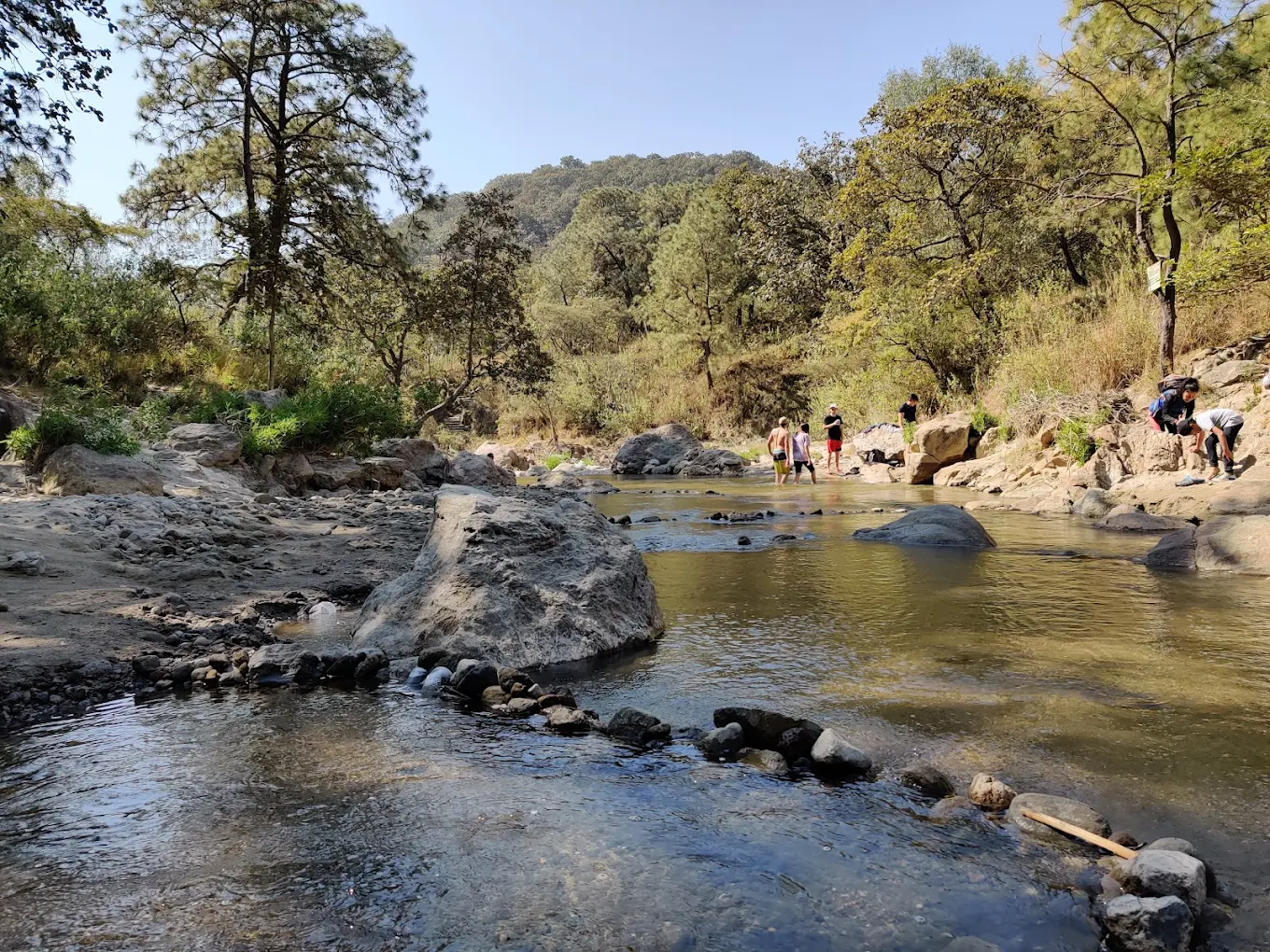 Río Caliente rodeado de árboles y visitantes disfrutando del entorno natural.