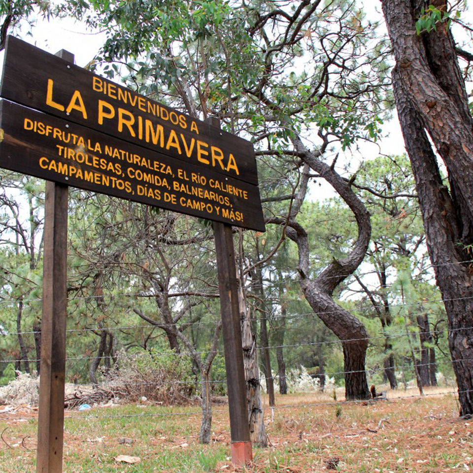 Letrero de bienvenida a La Primavera invitando a disfrutar de la naturaleza y el Río Caliente.