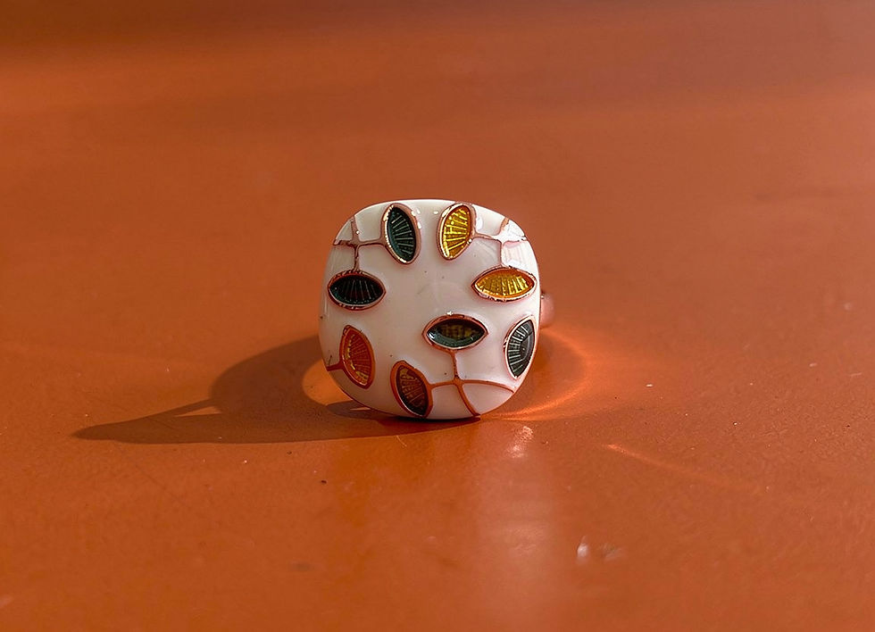 Annasach The Maaya ring, white enamel dome with mosaic leaf pattern in olive, mustard and slate enamel, on orange background
