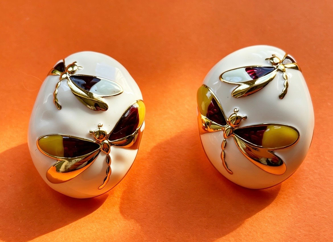 A pair of The Evelyn White Enamel Dragonfly Earrings with a domed white enamel design and gold dragonfly motif.