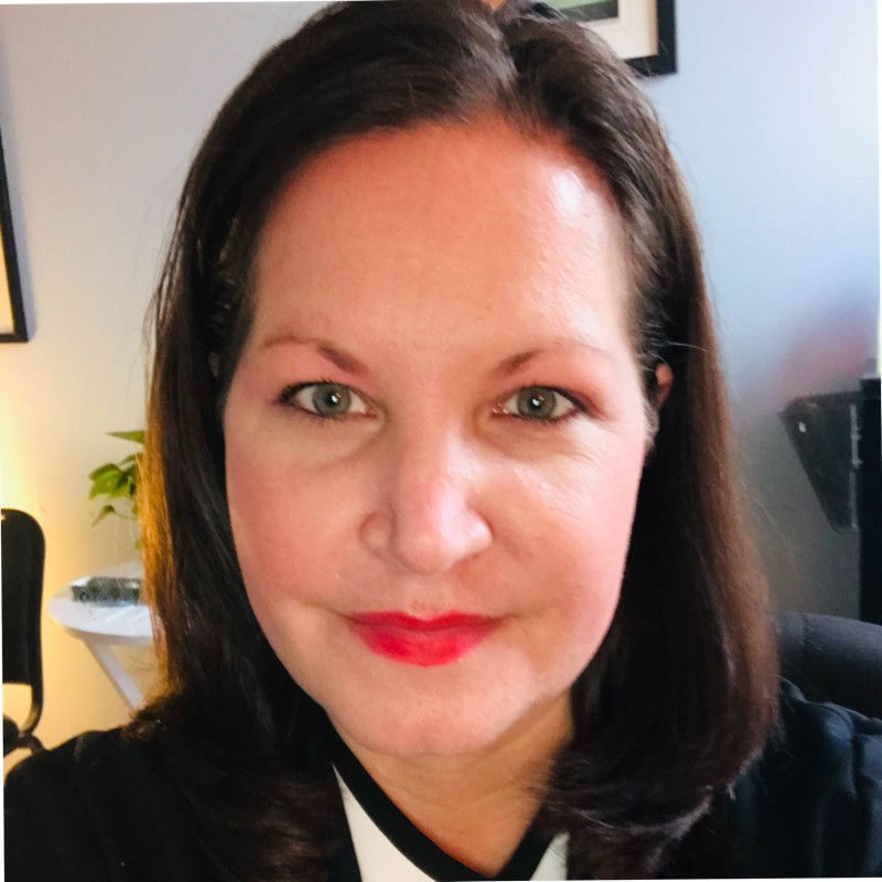 Jill O’Neill, a guest on episode 11 of The Legal Mindset Corner podcast, smiles warmly at the camera. She has shoulder-length dark hair and is wearing a black top with red lipstick, set against a light-colored background.