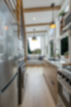 Bright tiny home on wheels with modern kitchen, large windows, built-in sofa, and space-saving ladder to loft, available for delivery across the US and Canada.