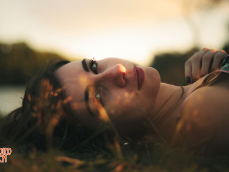 Woman lying in golden grass at sunset, eyes open to the sky — somatic grounding for anxiety, coming back to the body and the earth