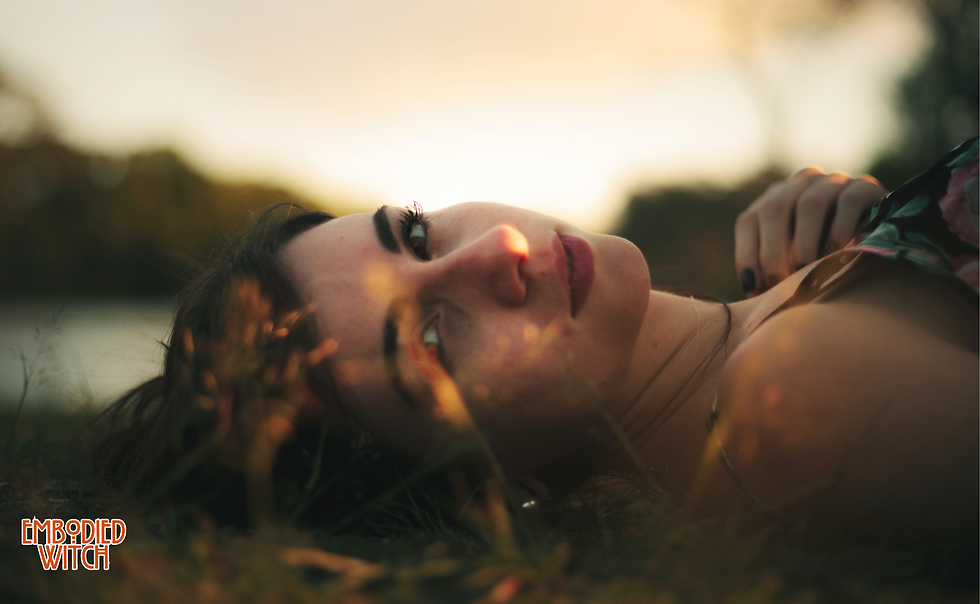 Woman lying in golden grass at sunset, eyes open to the sky — somatic grounding for anxiety, coming back to the body and the earth