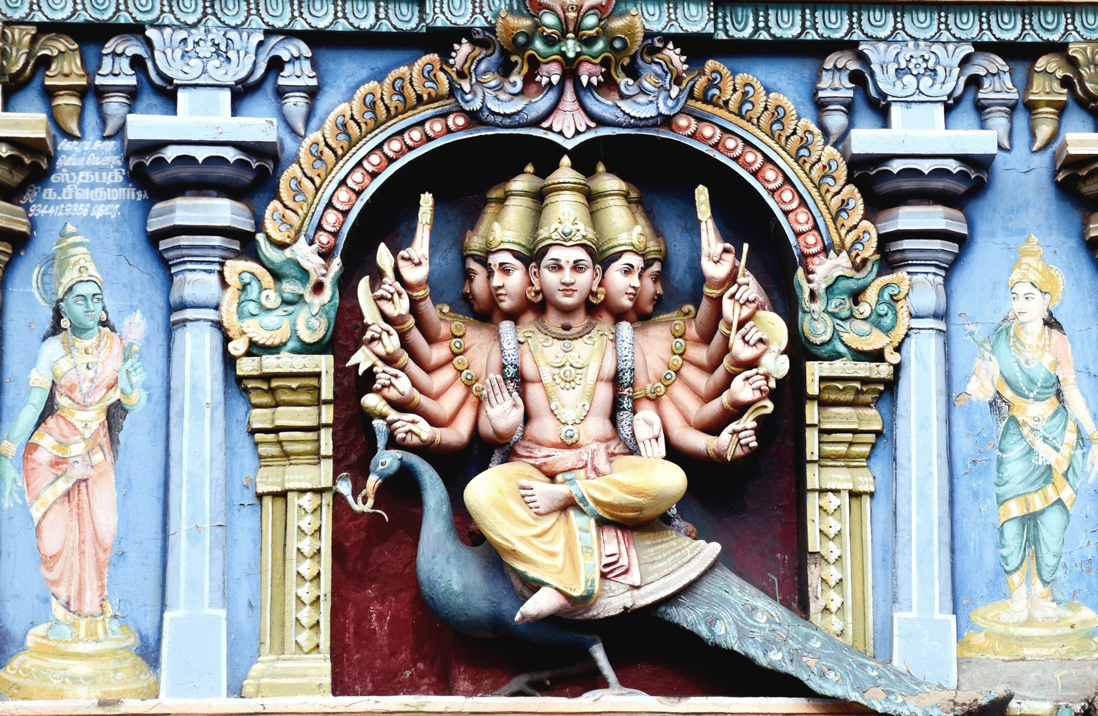 Six-headed deity with many arms riding a peacock