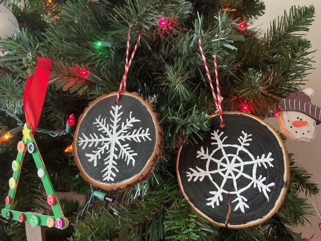 Wood slice ornaments with painted snowflakes hanging on a tree.