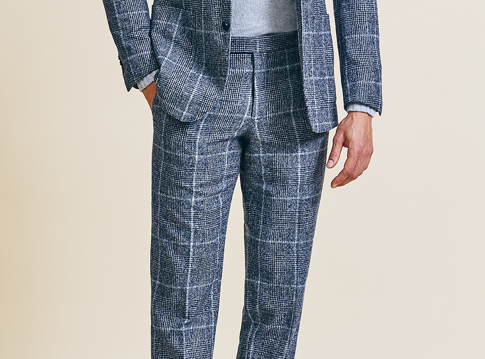 A man in a blue checked patterned suit with a light gray turtleneck, complemented by navy suede shoes, showcasing a bold and contemporary take on formalwear.