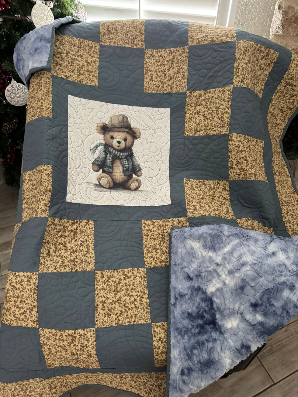Close-up of handmade quilt with a cowboy teddy bear fabric panel in the center, surrounded by gold and slate blue