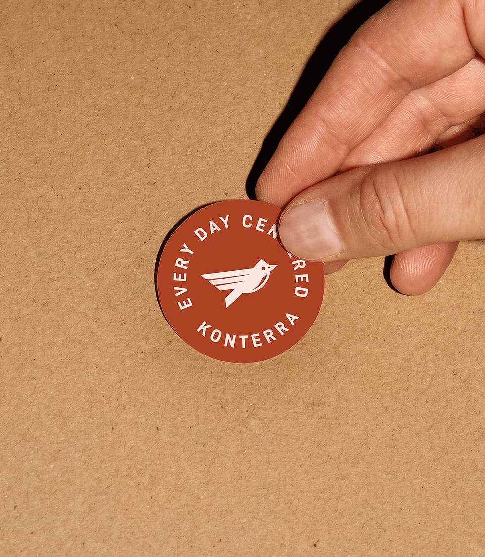 A hand placing a branded sticker that features the mascot and tagline "Every Day Centered"