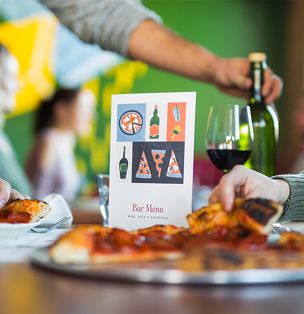 A bar menu standing upright on a table set with pizza and wine