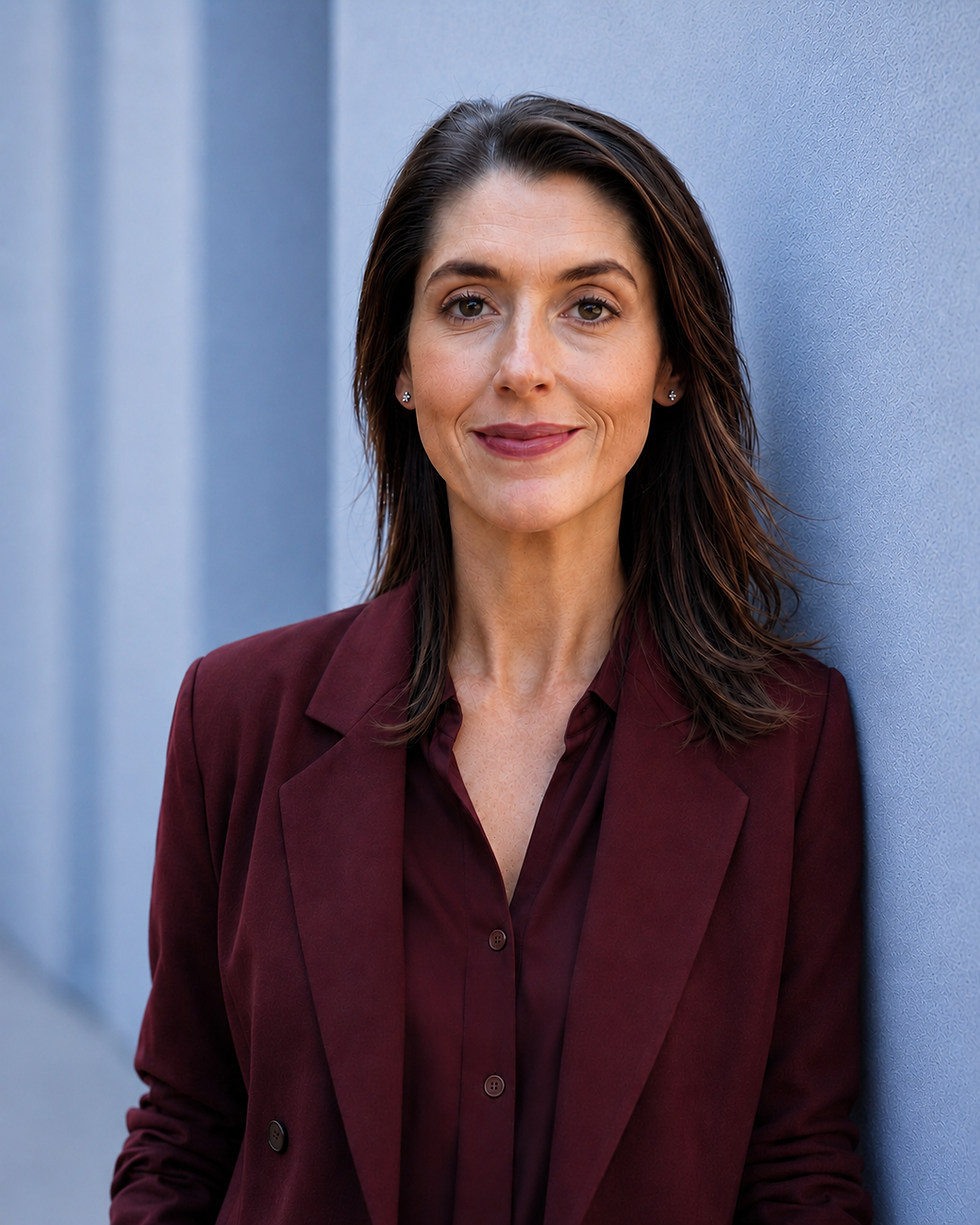 Melinda Welch leans against a blue wall wearing a oxblood dress shirt and suit jacket