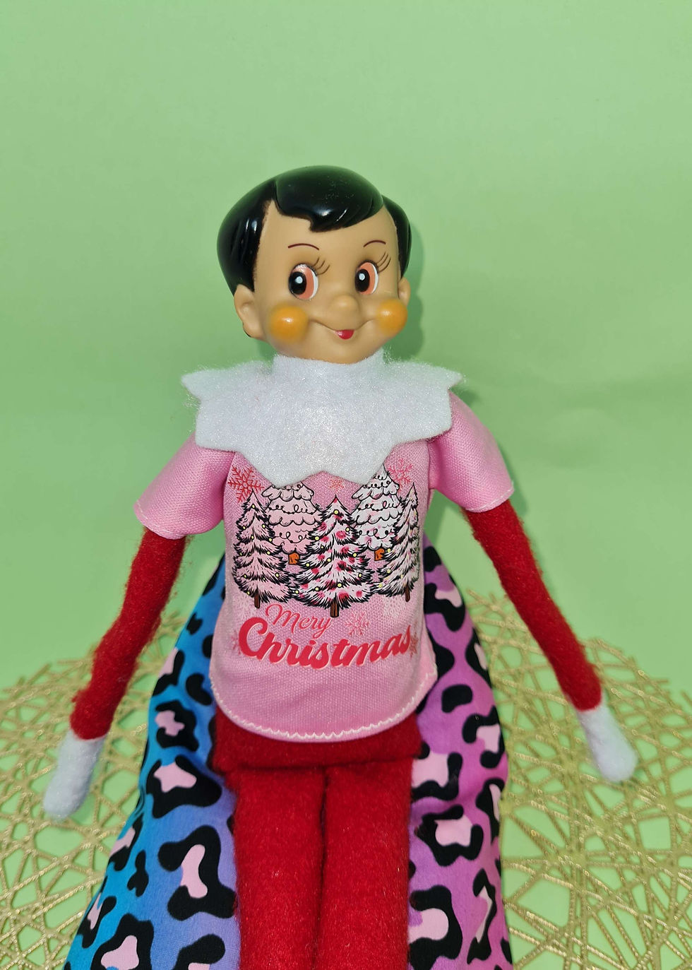 Elf On The Shelf doll posing in Christmas themed tshirt in pink
