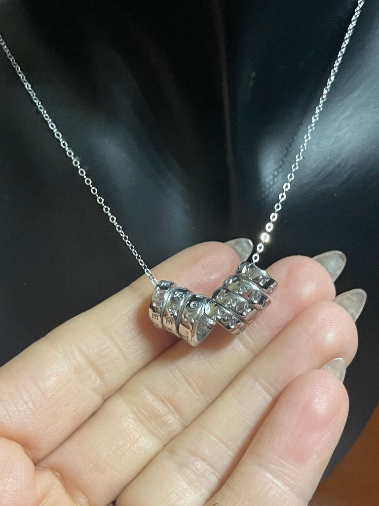 Thumbnail: a hand holding a silver scroll necklace with 2 scrolls on a delicate chain