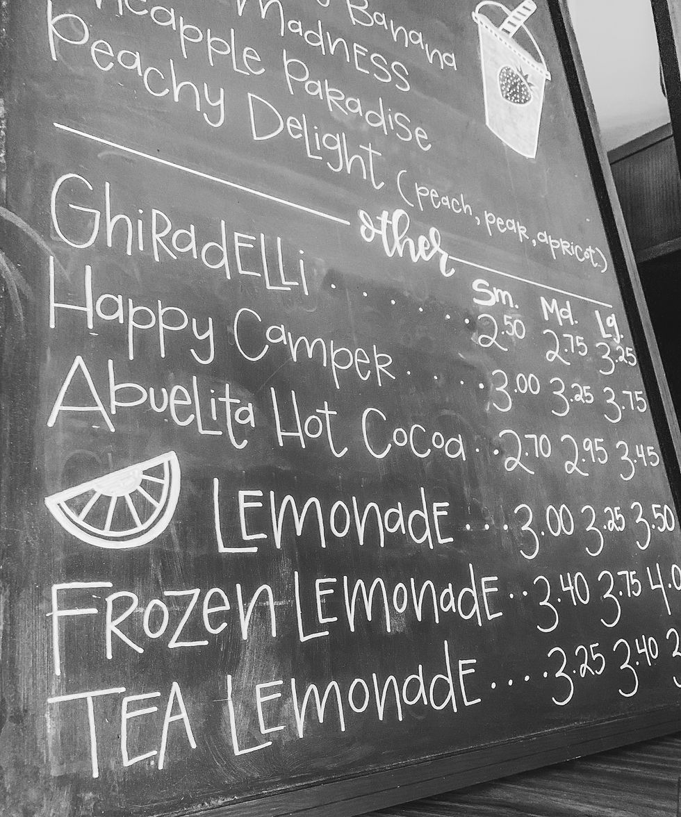 Hand-lettered chalkboard menu at a local Iowa coffee shop, featuring custom calligraphy drink listings created by Letters from Elliott, including lemonade, hot cocoa, and Ghirardelli specials.