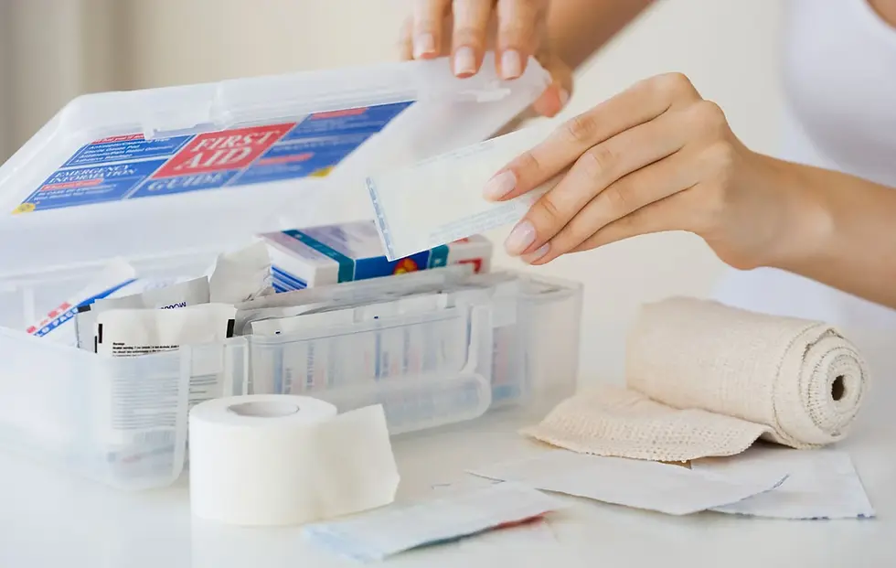 An open first aid kit with bandages, gauze, sterile wipes, and tape on a white surface. The kit's lid shows "FIRST AID." with a person organising supplies, making sure the kit is fully equipped.