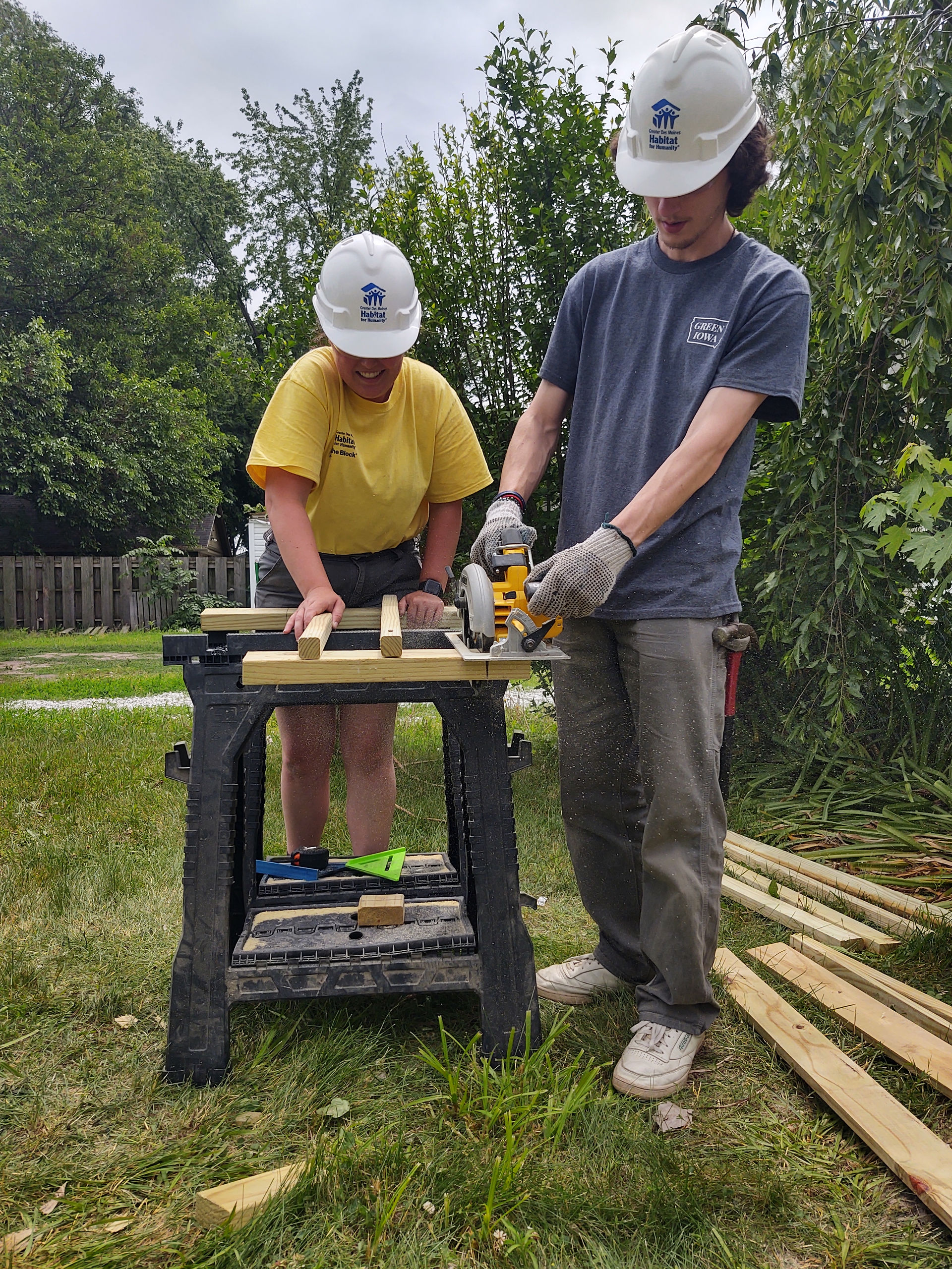 Woman in yellow shirt helping man in blue shirt use circular saw