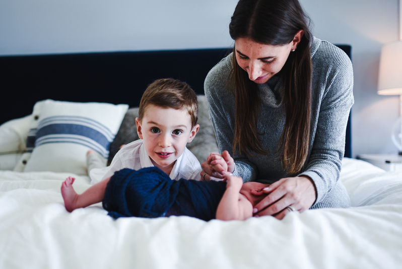 mom and brother with newborn on bed