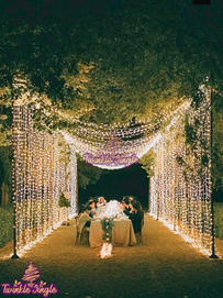 outdoor draped and hanging over head fairylights with long table centre piece of white flower bouquets with tea candles for wedding dinner for family