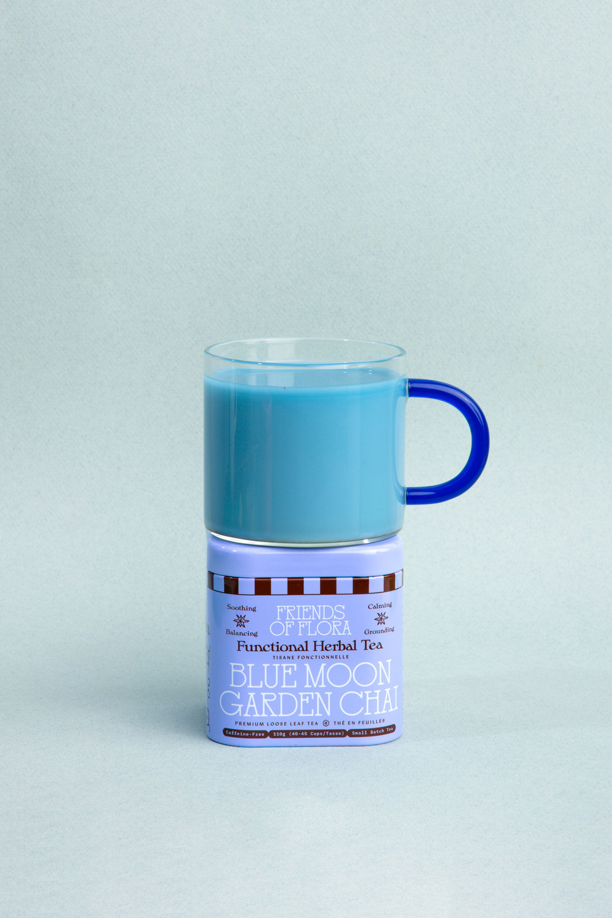 Closed tin of Blue Moon Garden Chai with a brewed cup of butterfly pea flower chai on top