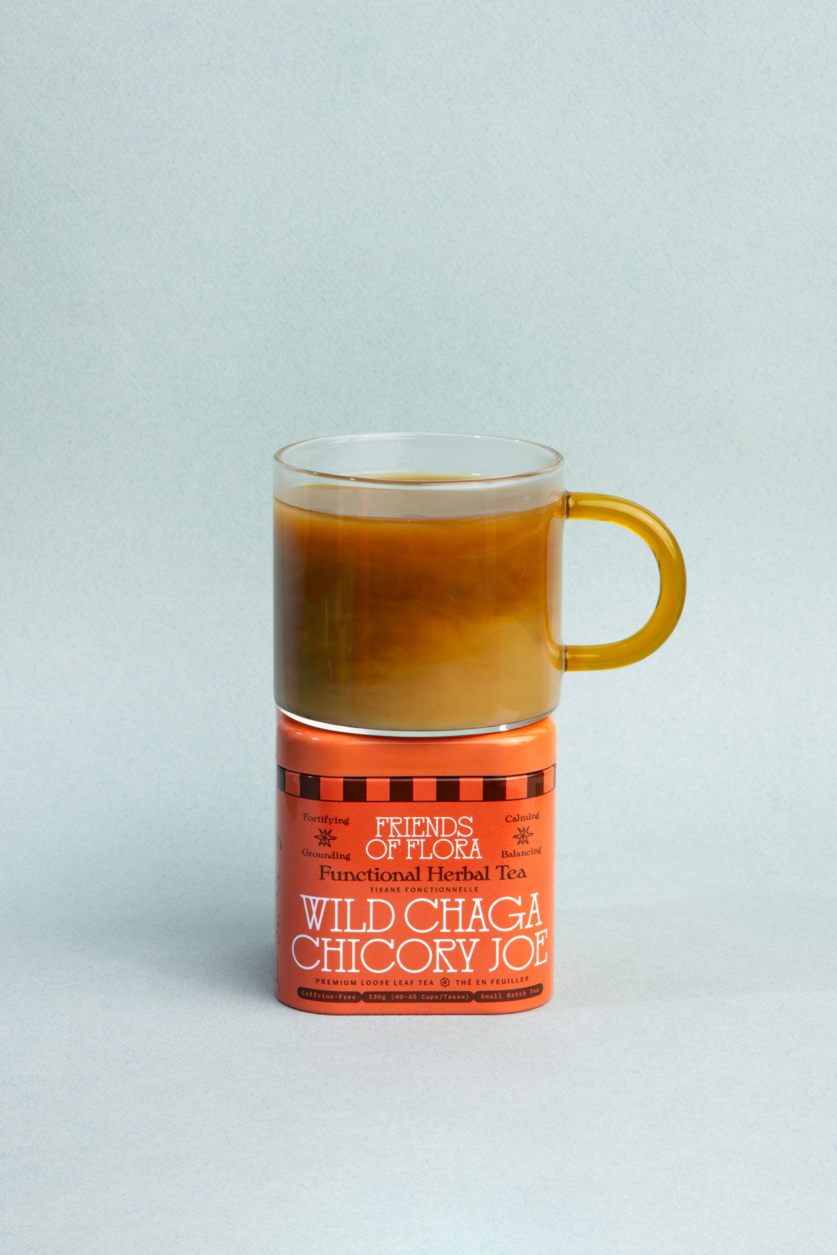 Closed aluminum tin of Wild Chaga Chicory Joe with a cup of brewed herbal tea stacked on top