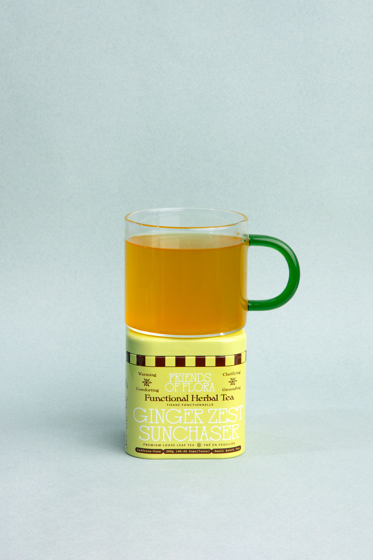 Closed tin of Ginger Zest Sunchaser with a brewed cup of tea on top against a blue background
