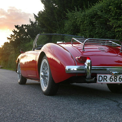 A red vintage car heading towards a sunset