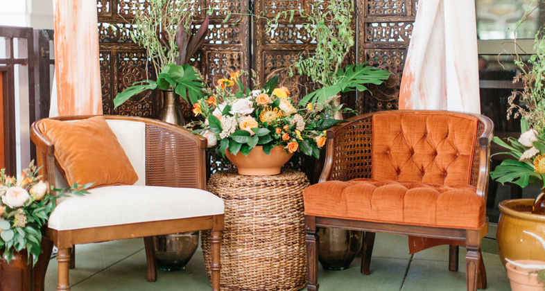 Two chairs with decorative setup including flowers, plants and a wooden  divider with drapes