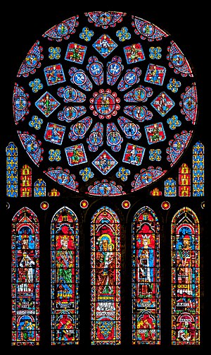 A large, majestic Gothic stained-glass window arrangement set against a pitch-black background, composed of a massive circular rose window positioned above five tall, narrow lancet windows.