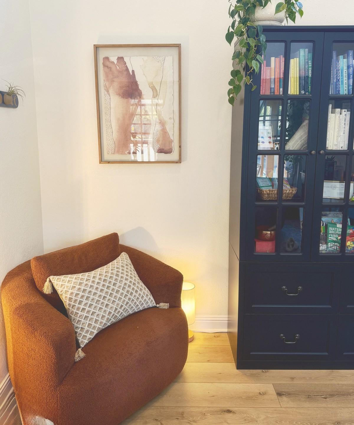 A cozy corner of my Carmel office with a rust-colored chair, a watercolor print, and a tall bookcase