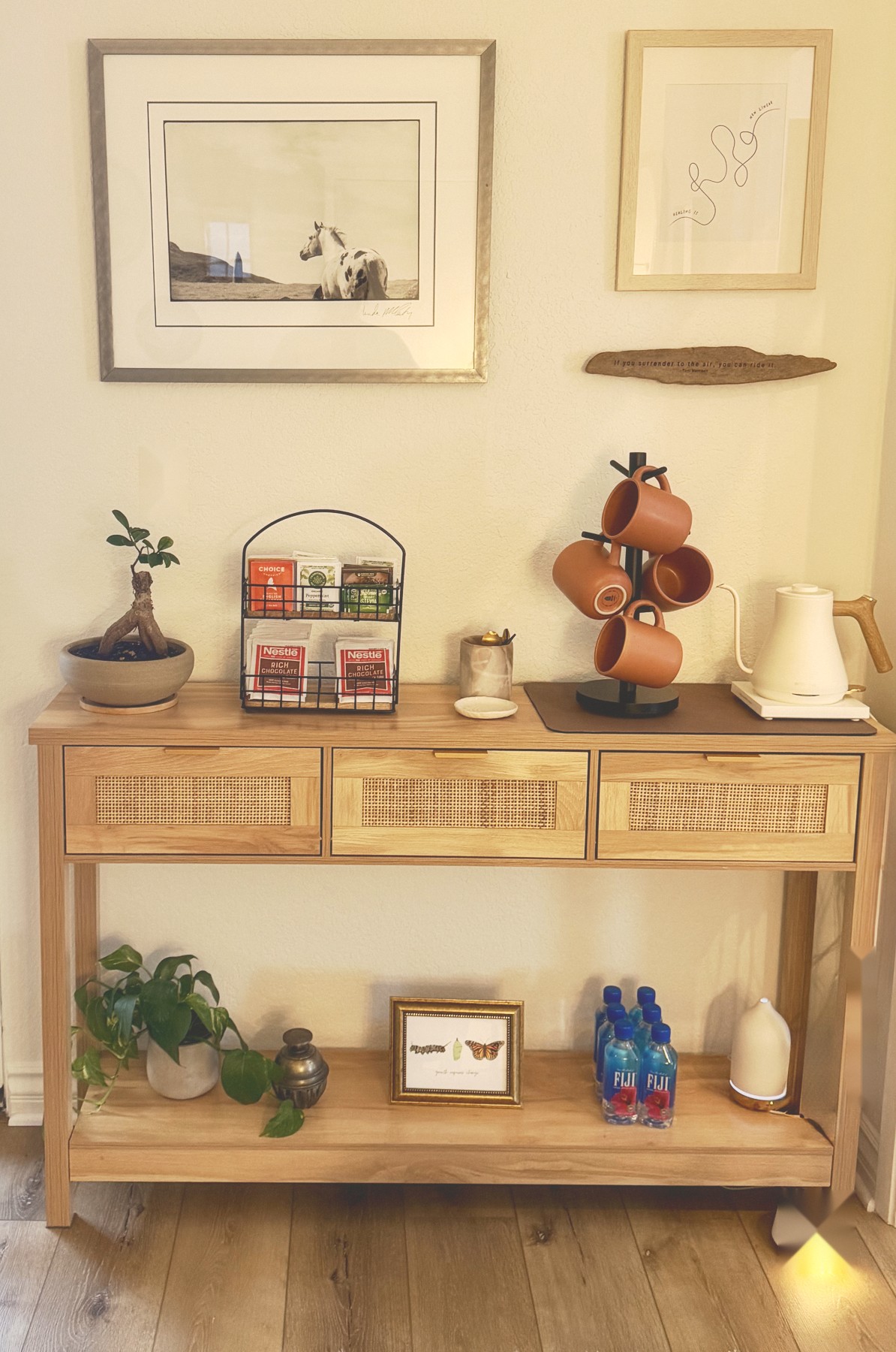 A table in my office with framed art, a tea and coffee station, and a small plant