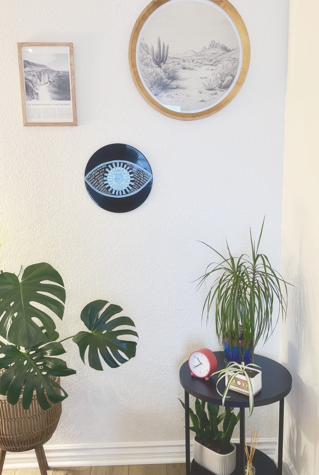 Plants, framed art, and a round desert print on a wall in my office