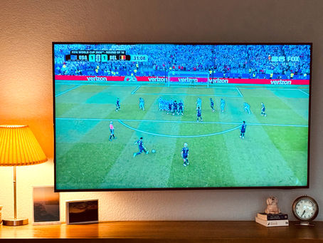 TV screen showing a soccer game (USA v Belguim).  The TV is next to a lamp and above a cabinet with some decor.