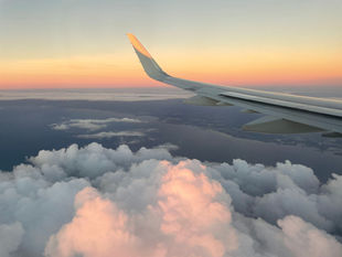 Wing of an airplane above puffy clouds during sunset