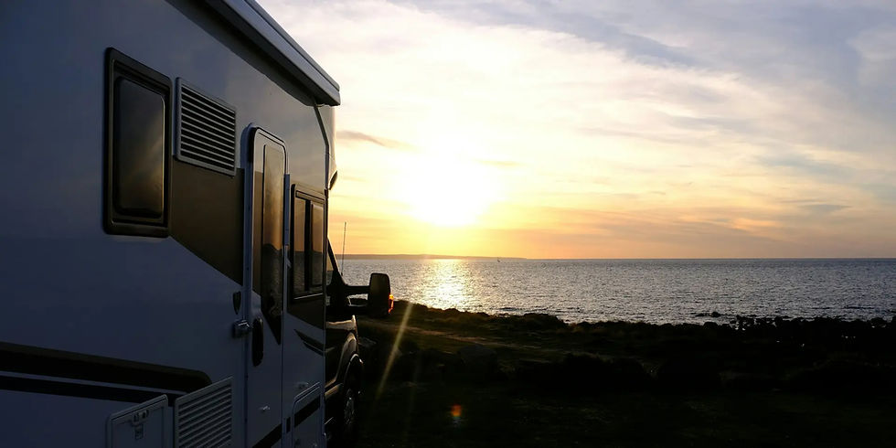 Camping-car stationné au bord de la mer sous un coucher de soleil doré. Ciel partiellement nuageux et ambiance sereine.