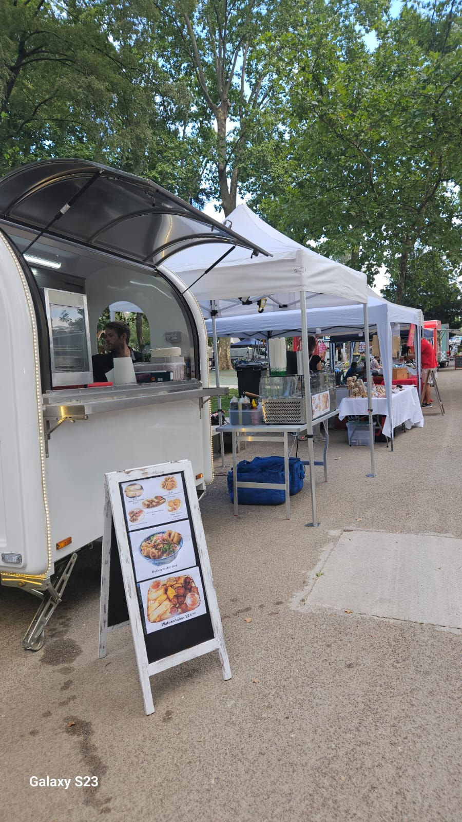 Photo du food truck Asia Lune sur un marché, paysage, couleurs naturelles, met en avant le stand et le menu affiché devant.