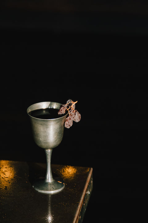 Deep purple cocktail served in a brass goblet with muscatels.