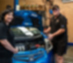 Two technicians inspecting a blue car in a repair shop