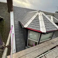 Grey slate roof with a bay window featuring white lead flashing and wooden scaffolding