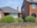 A small brick house with white trim with a large shrubbery in front