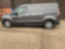 A grey van is parked beside a building with red brick and brown panelling